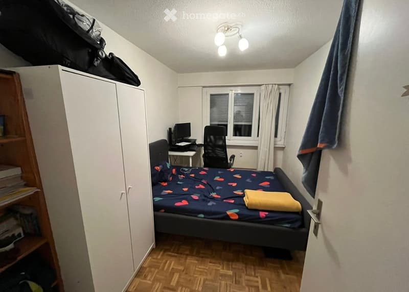 Cozy bedroom with a double bed, desk, chair, wardrobe, and window with curtains.