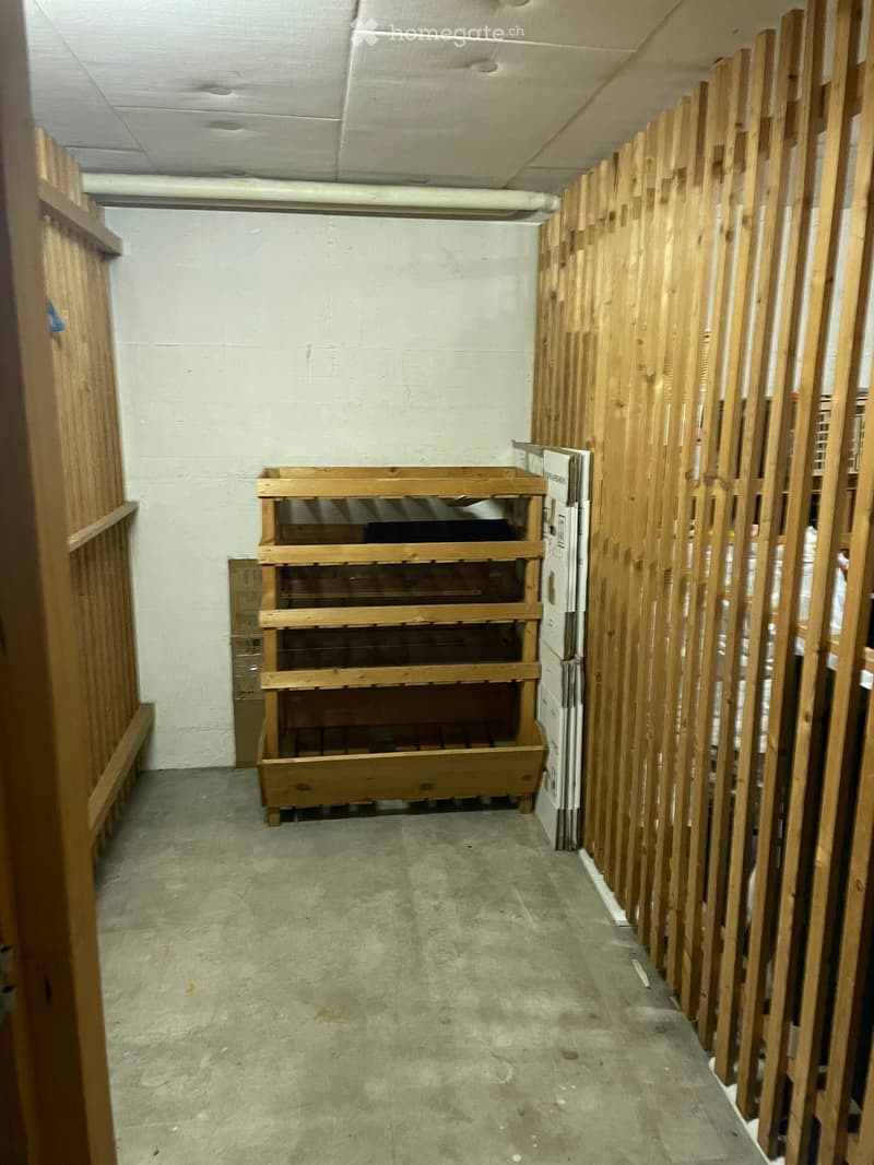 Empty room with concrete floor, white walls, and wooden shelving units along one wall.