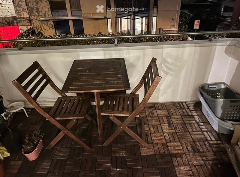 Balcony with wooden decking, small table, two folding chairs, and a laundry basket.