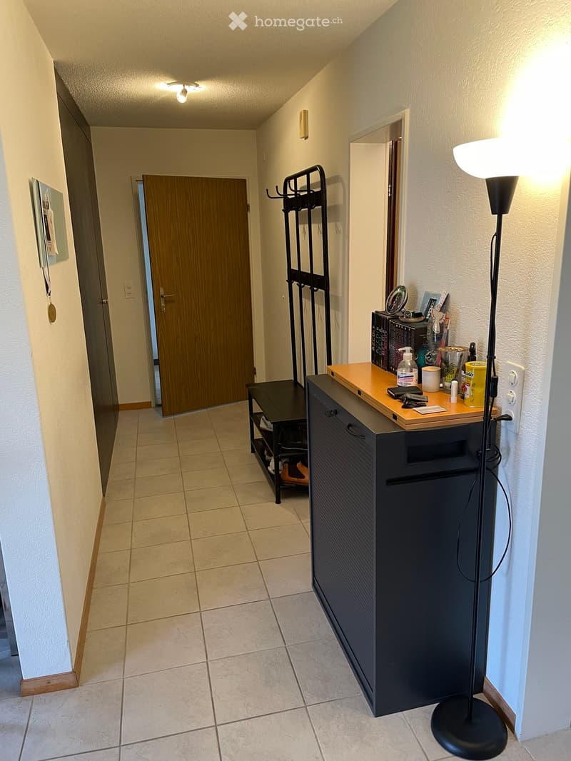 Hallway with tiled floor, wooden door, coat rack, small table with items, and floor lamp.