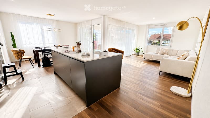 Open-plan living and dining area with modern furniture, a kitchen island, and large windows with sheer curtains.