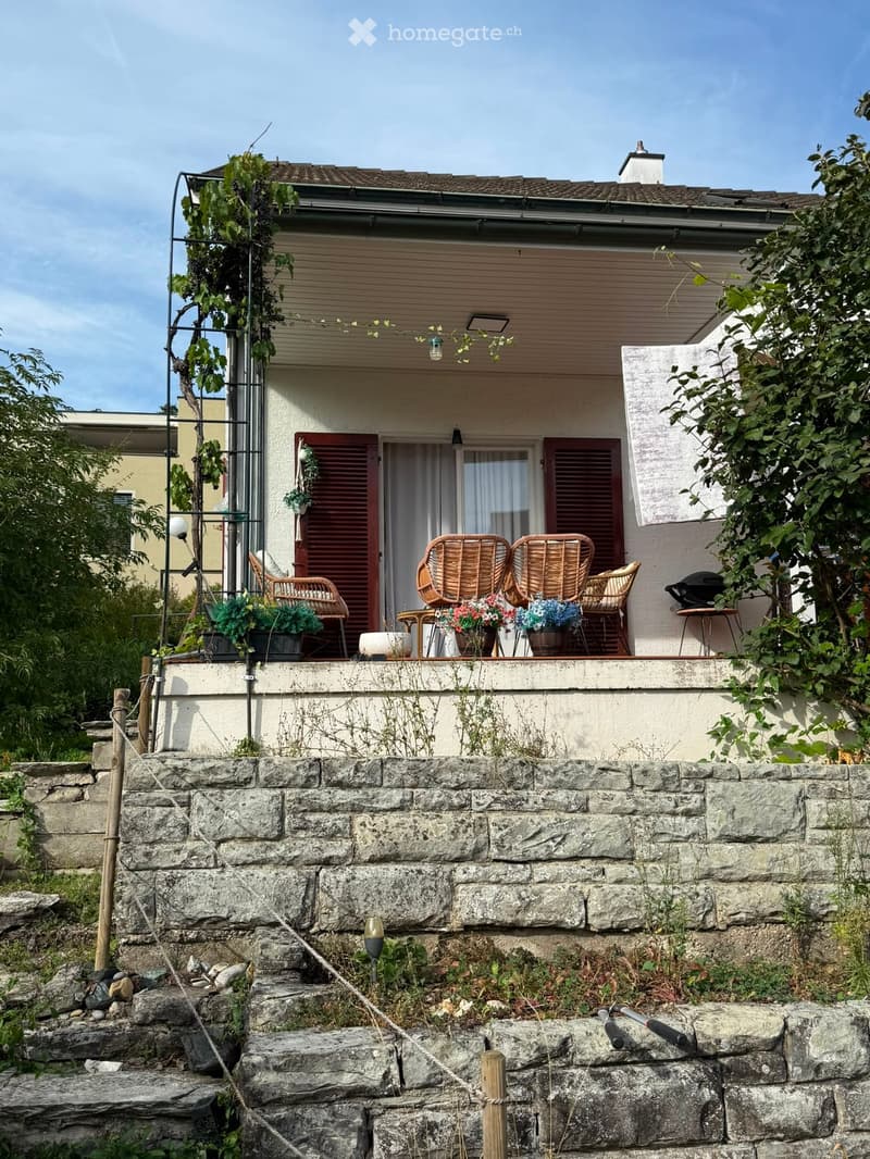 Balcony with wicker chairs, small table, flower pots, and a stone staircase leading up to it.
