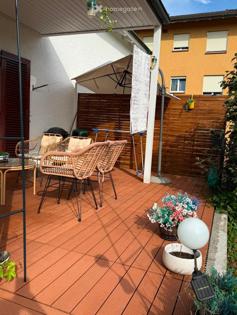 Balcony with wooden decking, wicker chairs, small table, flower pots, and an umbrella.