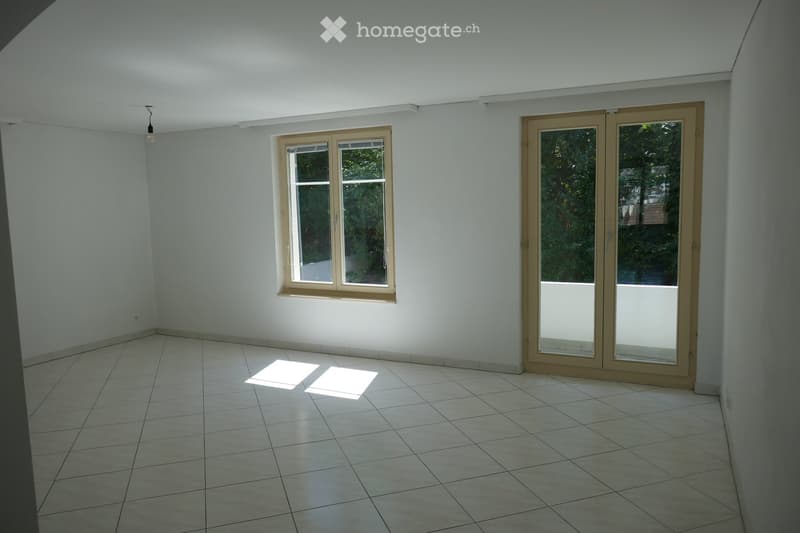 Empty room with tiled floor, white walls, and two windows, one of which is a sliding glass door leading to a balcony.