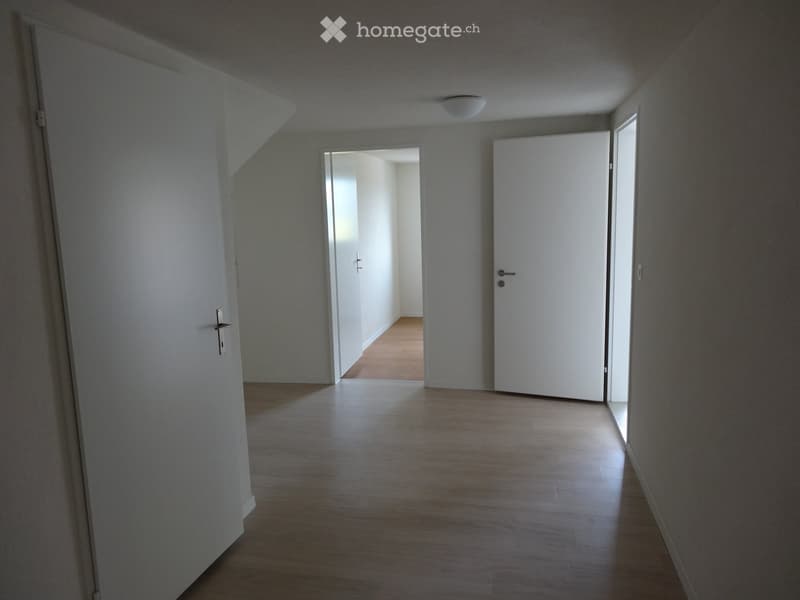Empty hallway with wooden flooring, white walls, and two doors leading to other rooms.