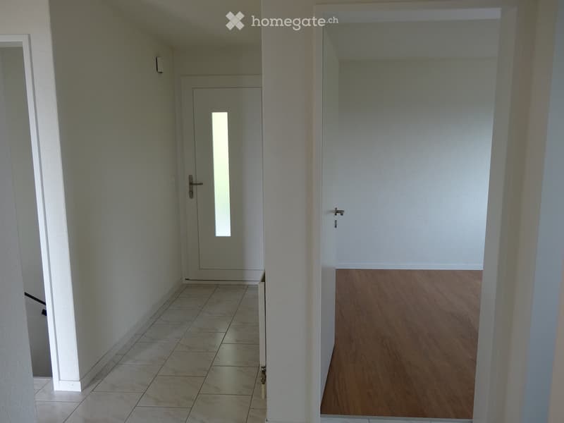 Empty hallway with tiled floor on left and wooden floor on right, featuring two doors and a mirror on the left wall.