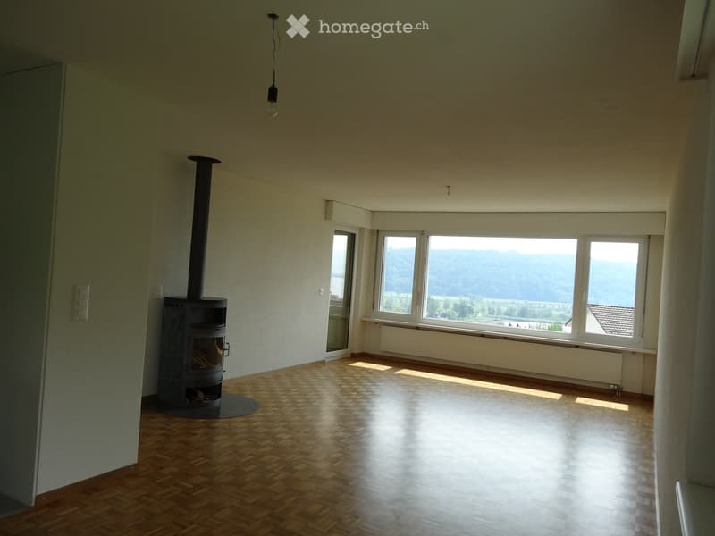 Empty room with wooden flooring, large windows offering a scenic view, and a fireplace with a chimney.