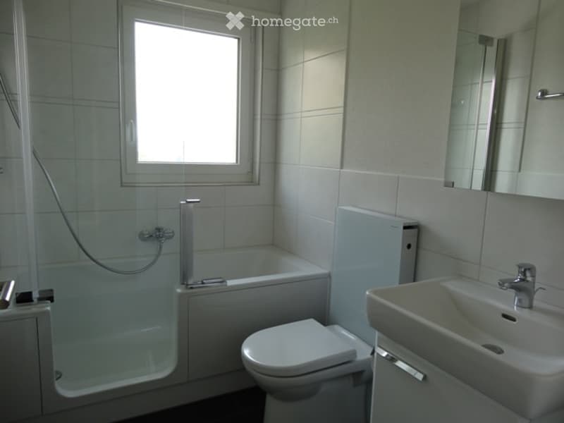 Modern bathroom with white tiles, a bathtub, toilet, sink, and a large mirror above the sink.