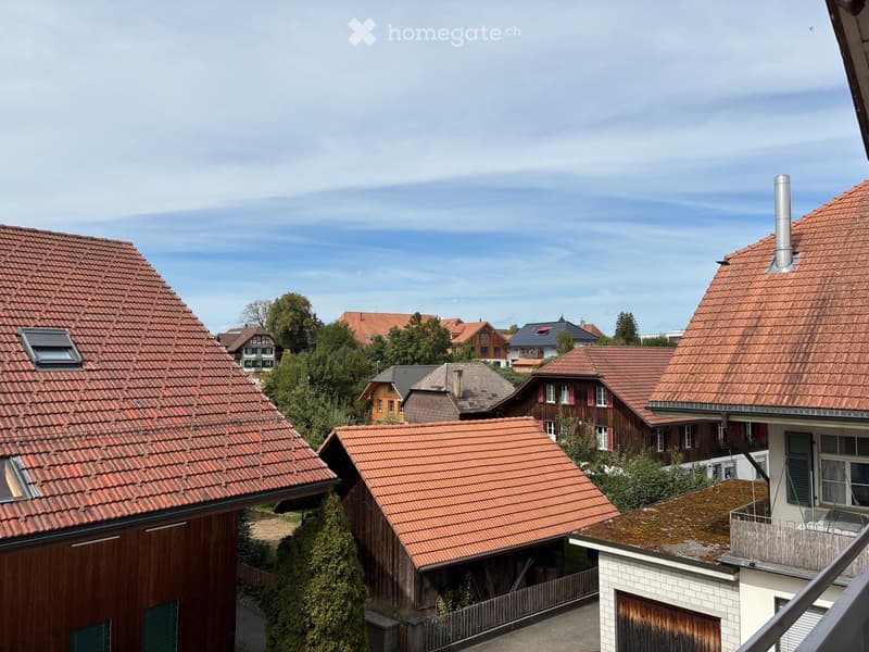 A view of several residential houses with red-tiled roofs, surrounded by trees and greenery under a partly cloudy sky.