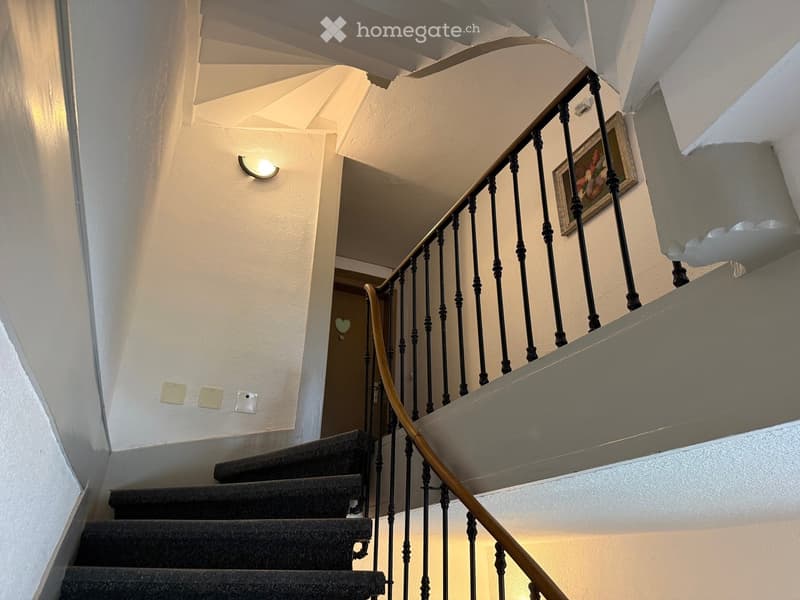 Spiral staircase with black wrought iron railing and wooden handrail, carpeted steps, wall-mounted light fixture, and a framed picture on the wall.