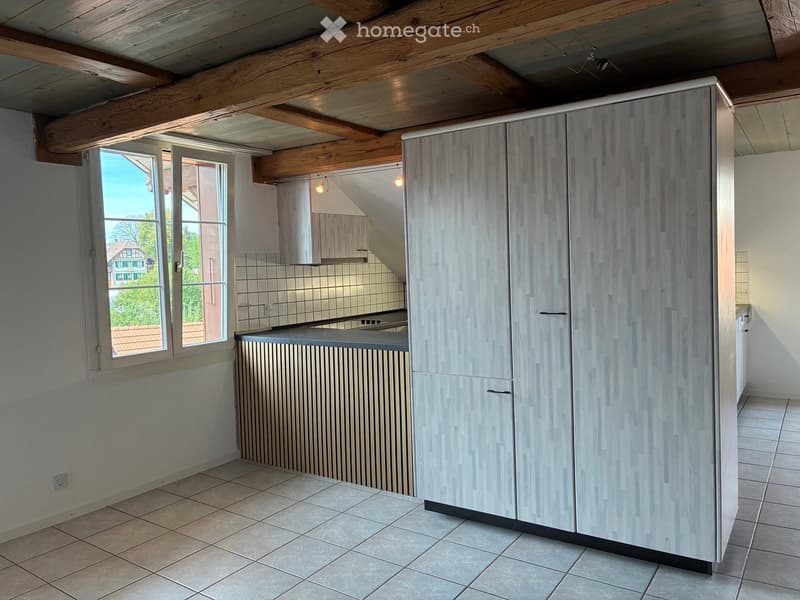 Modern kitchen with light-colored cabinets, a countertop, and large windows offering a view of the outside. The space features exposed wooden beams on the ceiling and tiled flooring.