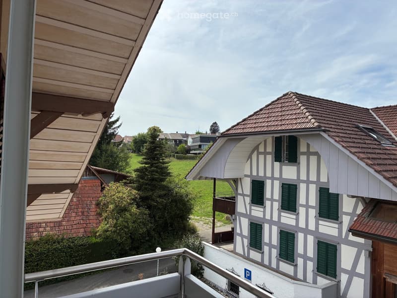 View from a balcony showing a traditional half-timbered house with green shutters, surrounded by greenery and other residential buildings.