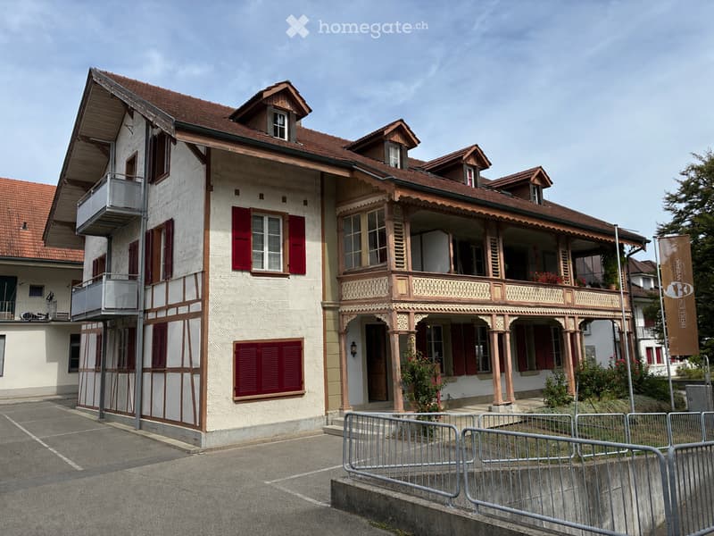 A multi-story building with a traditional architectural style, featuring red shutters, wooden balconies, and a tiled roof.