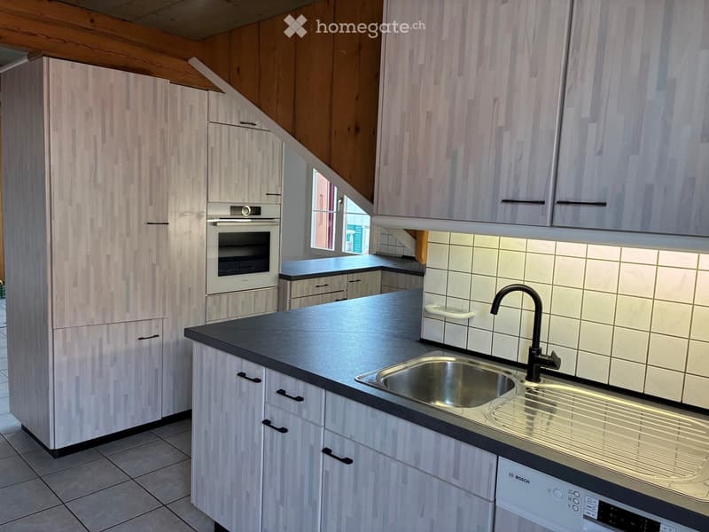 Modern kitchen with light wood cabinets, stainless steel sink, black countertop, and built-in appliances including an oven and dishwasher.