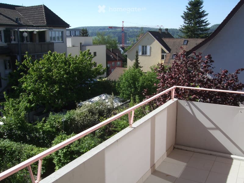 Balcony with tiled floor, white railing, overlooking a residential area with trees and houses.