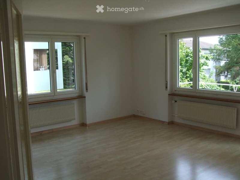 Empty room with wooden flooring, white walls, large windows, radiators, and a door leading to a balcony.