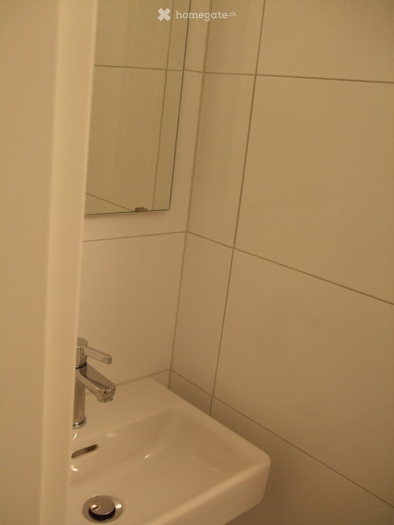 Modern bathroom with a white sink, chrome faucet, and a rectangular mirror mounted on beige tiled walls.