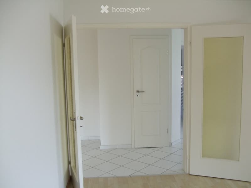 Empty hallway with white tiled floor, white walls, and multiple doors leading to other rooms.