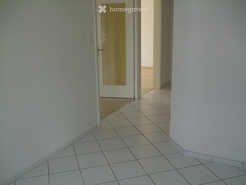 Empty hallway with tiled floor and white walls, featuring a closed door at the end.