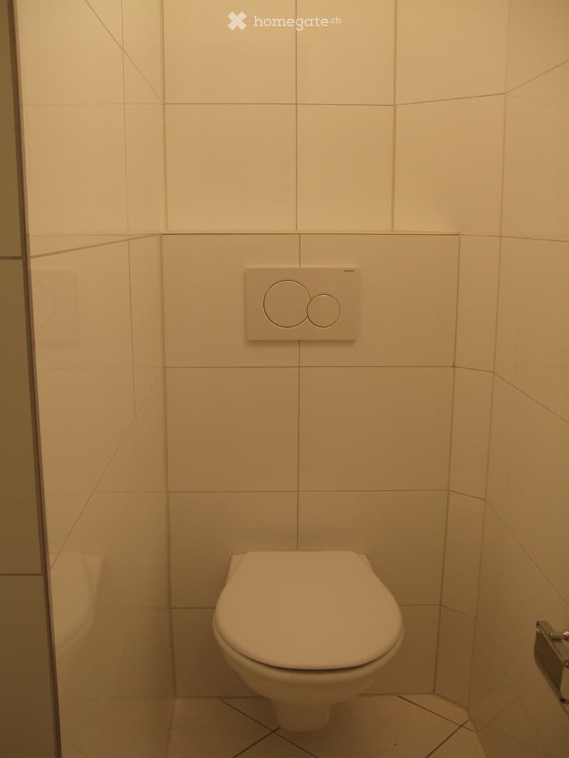 Modern bathroom with white tiled walls and floor, featuring a toilet and an electronic control panel above it.