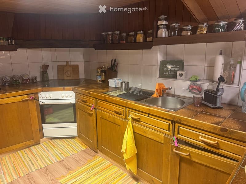 A cozy kitchen with wooden cabinets, a white oven, a sink with a faucet, and various kitchen items on the countertops and shelves.
