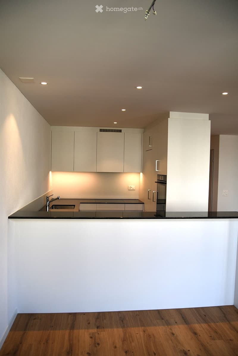 Modern kitchen with white cabinets, black countertop, and wooden flooring. Features a sink with a modern faucet and built-in lighting.