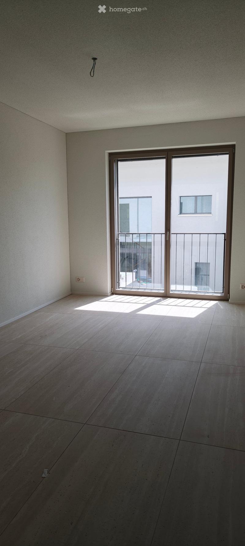 Empty room with light-colored tiled floor and white walls, featuring a large sliding glass door leading to a balcony.