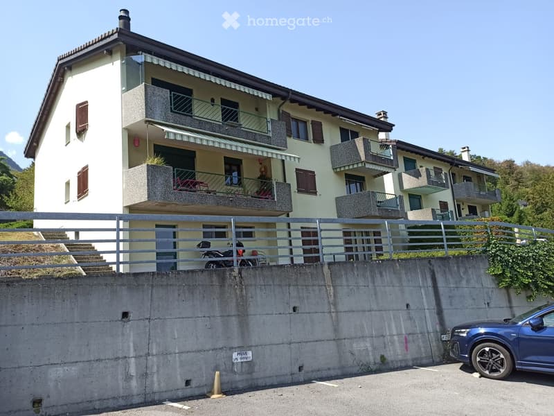 Two-story house with balconies, a raised ground floor, and a parking area.
