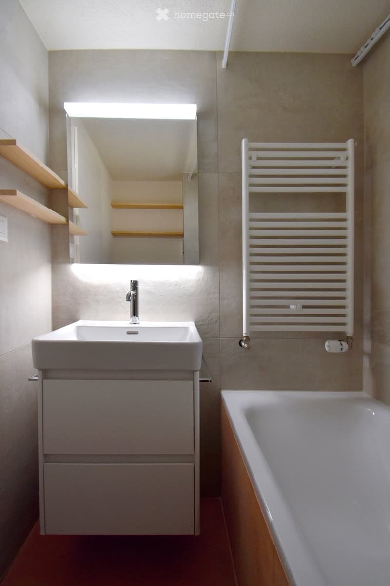 Modern bathroom with a white sink, chrome faucet, large mirror, bathtub, radiator, and wooden shelves.