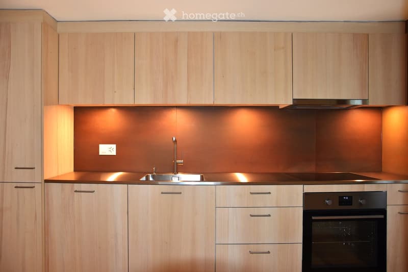 Modern kitchen with light wood cabinets, stainless steel sink, faucet, and built-in oven.