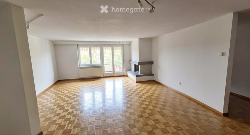 Empty room with wooden flooring, white walls, fireplace, large window, and sliding glass door leading to a balcony.