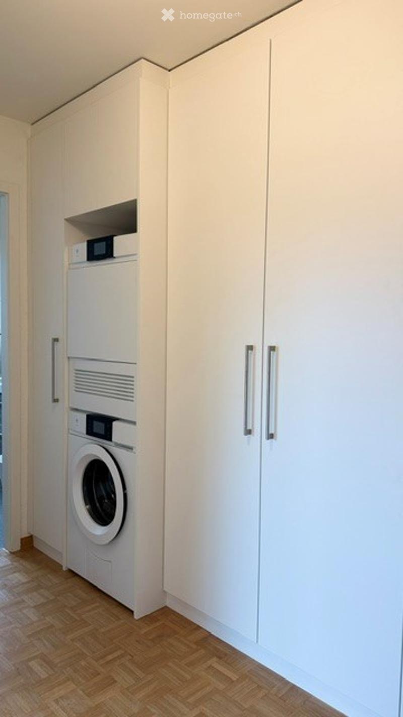 A compact, modern utility room with a white washing machine, built-in cabinets, and wooden flooring.