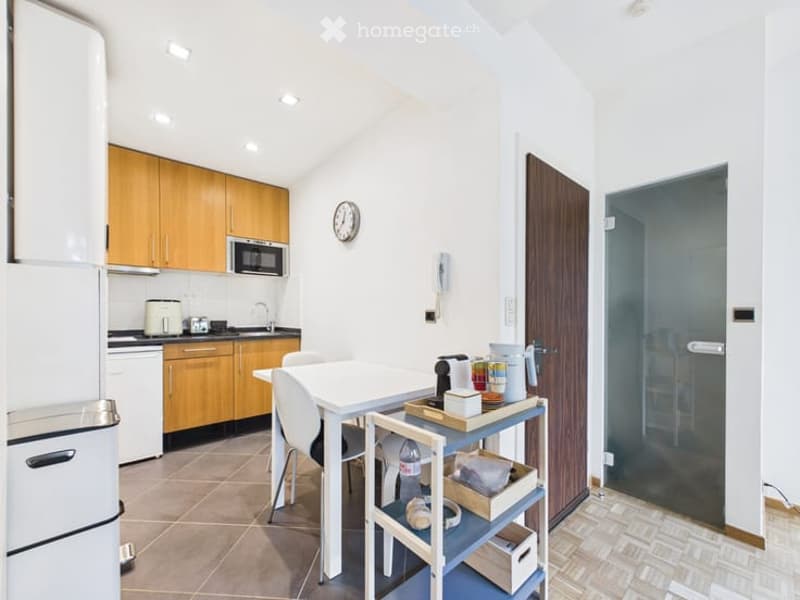 Modern kitchen with light wooden cabinets, stainless steel appliances, a white dining table with chairs, and a small cart with various items.