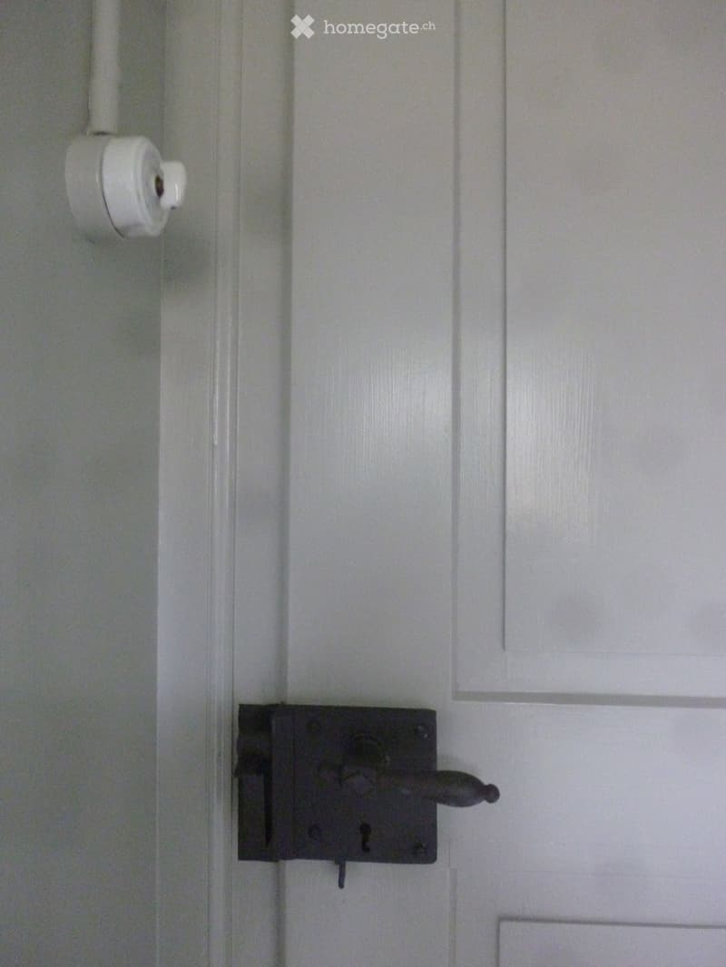 Close-up of a white interior door with a black handle and a small white thermostat or sensor mounted on the wall beside it.