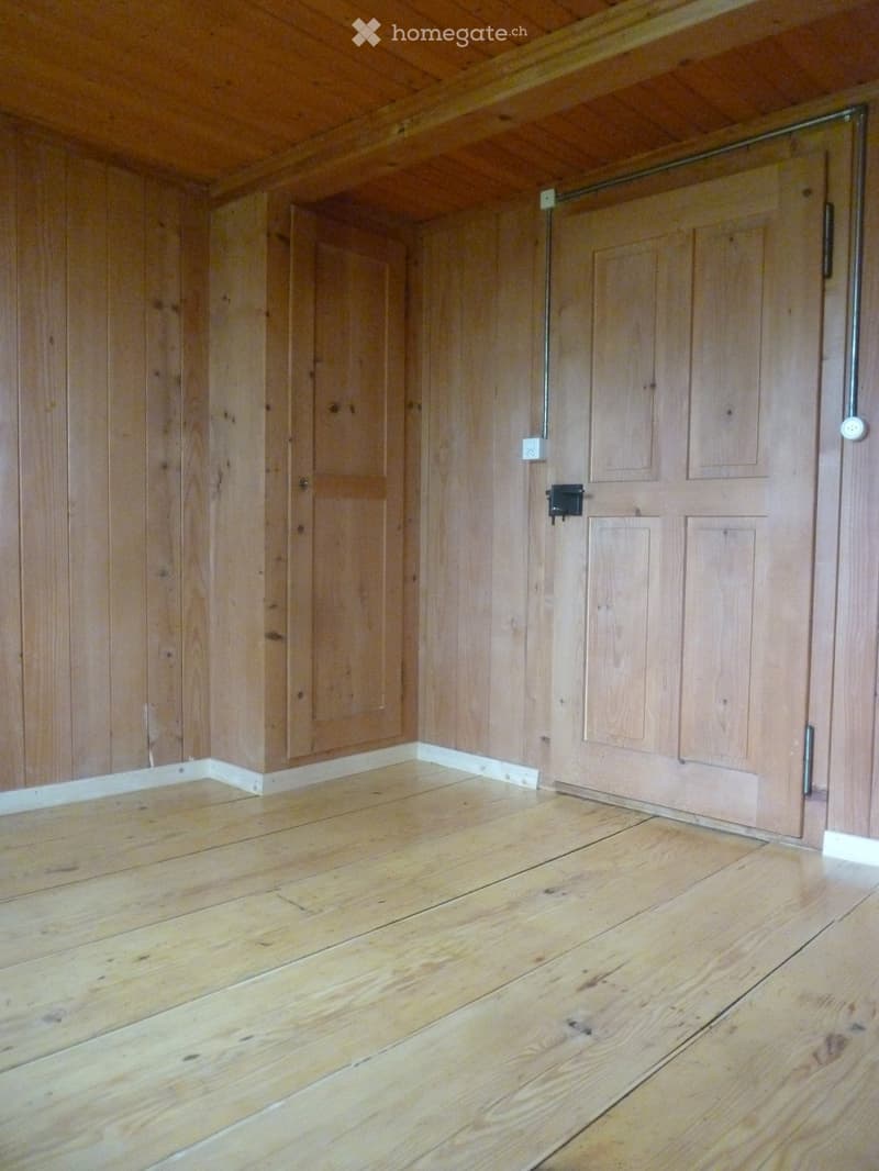 Empty room with wooden walls and floor, featuring built-in wooden cabinets and a sliding door.