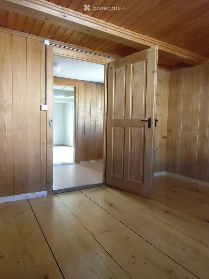 Empty wooden room with polished floor, wooden walls, and sliding barn-style doors leading to another room.