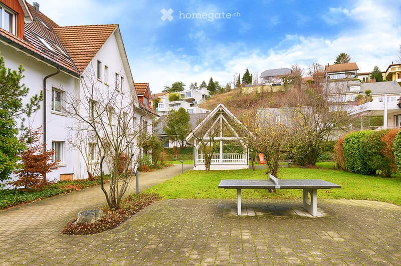 Residential outdoor area with a paved walkway, a small gazebo, a ping pong table, and surrounding greenery.