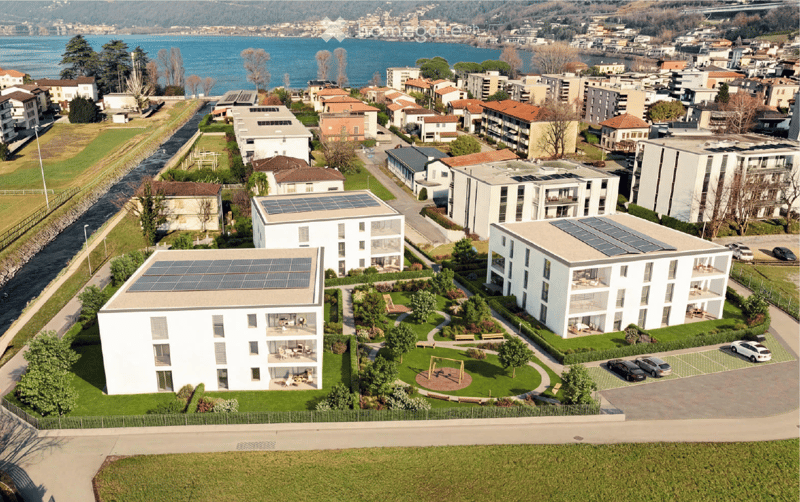 Multiple white buildings, solar panels on the roofs, lush green lawn, playground, parking lot, bodies of water