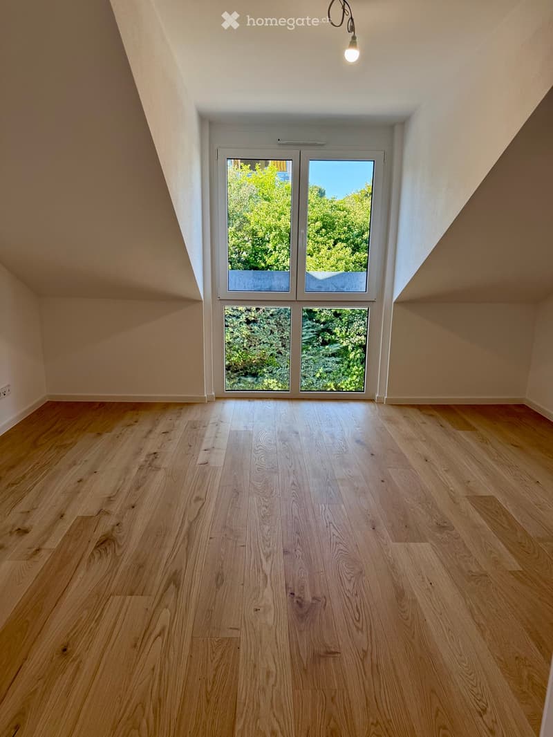 Empty room with wooden flooring, large windows, and a slanted ceiling.