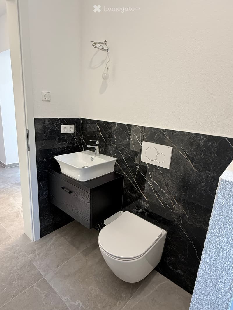 Modern bathroom with a white sink, toilet, and dark wooden cabinet, featuring black marble wall tiles and a sleek faucet.
