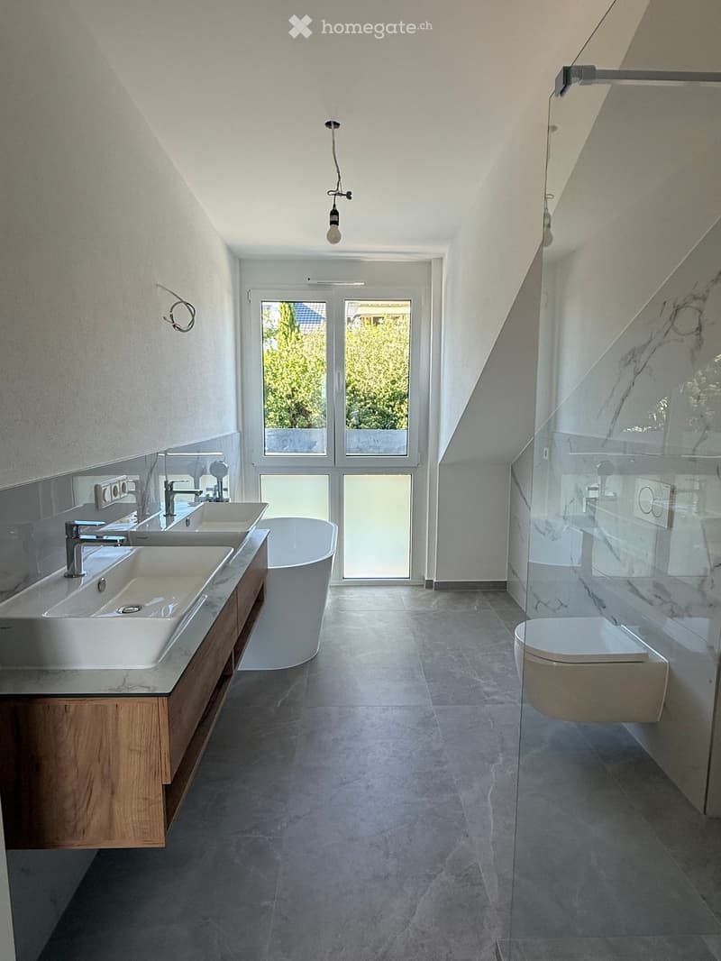 Modern bathroom with double sinks, a bathtub, and a toilet, featuring large windows and a glass shower enclosure.