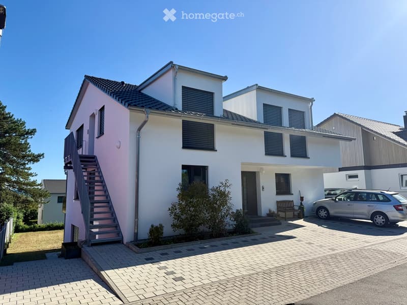 Two-story modern house with white and pink exterior, multiple windows, a staircase leading to the entrance, and a parked car in the driveway.