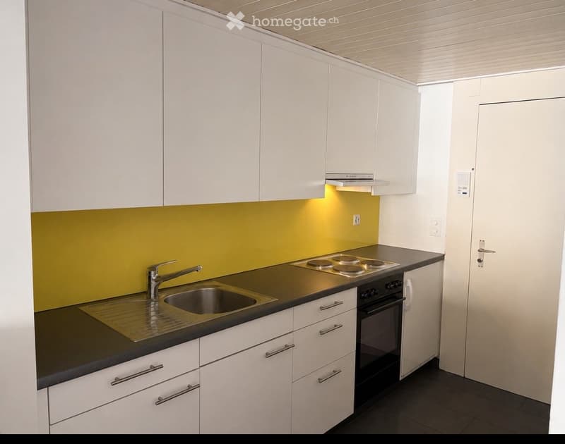Modern kitchen with white cabinets, black countertops, stainless steel sink, and built-in stove and oven. Bright yellow accent wall and sleek design.