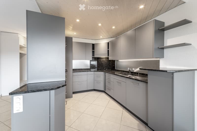 Modern kitchen with grey cabinets, dark countertops, and a sleek design. Features include a sink, faucet, and built-in storage with shelves.