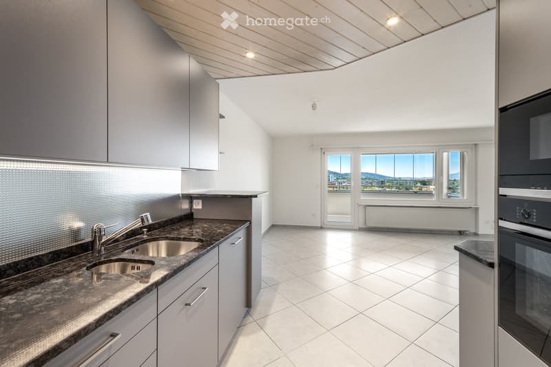 Modern kitchen with white cabinets, granite countertop, stainless steel sink, and built-in oven. Large windows offer a scenic view.
