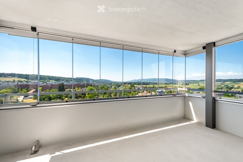 Empty room with large windows offering a panoramic view of the city and surrounding landscape. The space features white walls, a concrete floor, and modern architectural elements.