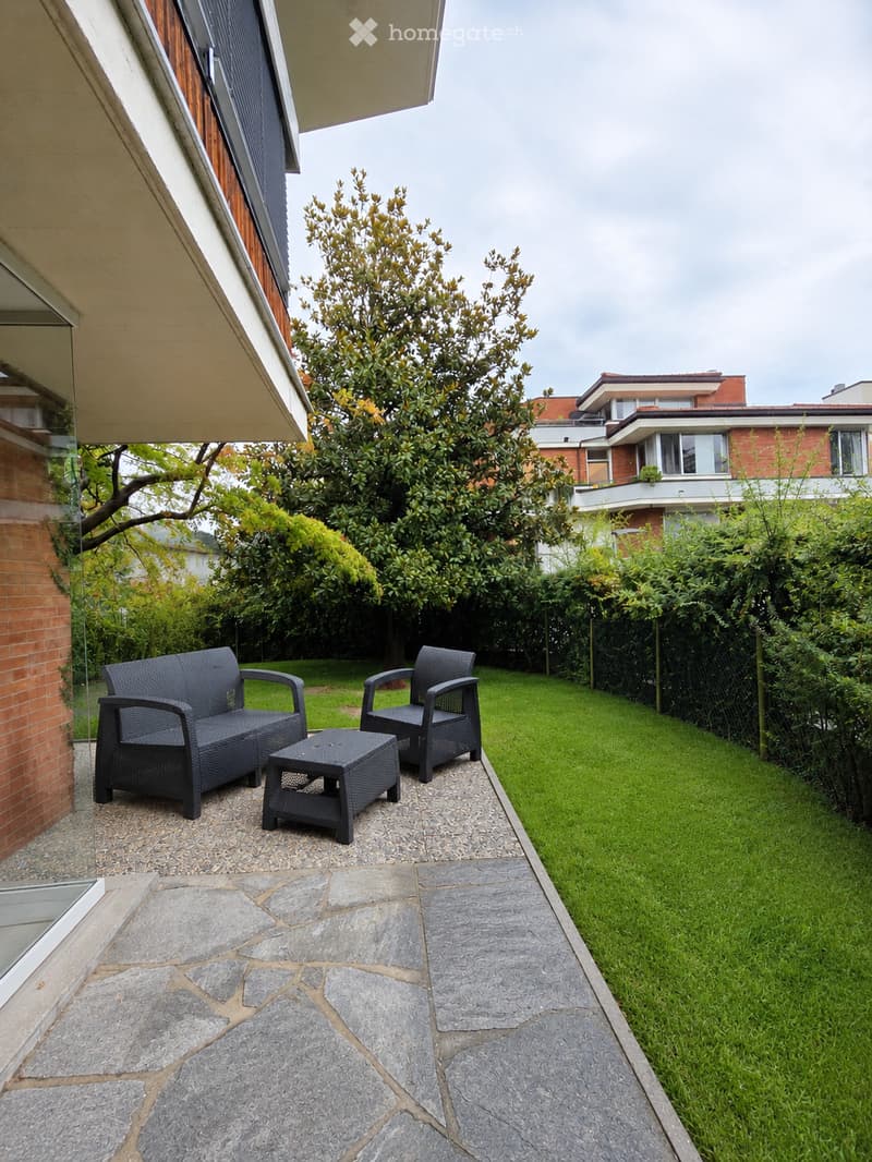 Garden area with a stone-paved pathway, green lawn, and outdoor seating including a sofa, chair, and table.