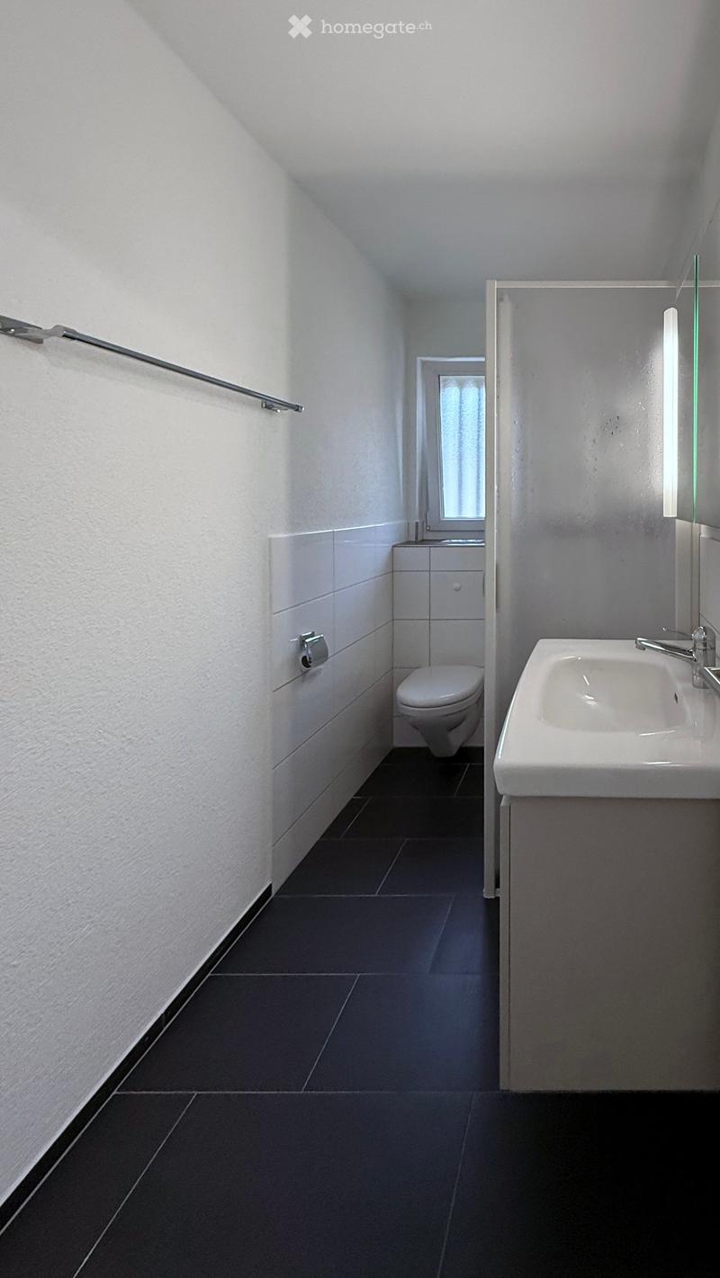 Modern bathroom with white tiles, dark floor, sink, toilet, and mirror.