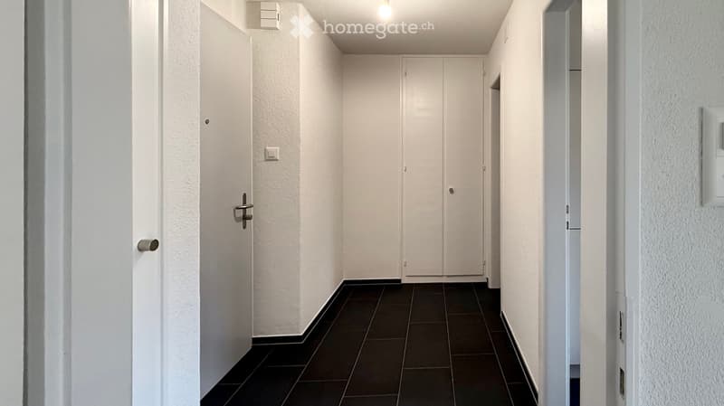 A narrow hallway with white walls, dark tiled floor, and closed white doors on both sides.