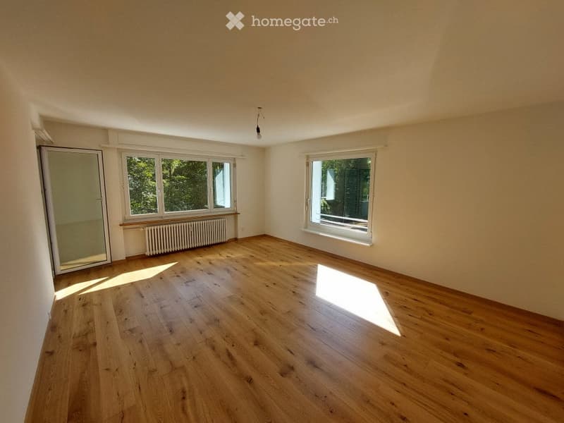 Empty room with wooden flooring, large windows, and a radiator. No furniture or equipment present.
